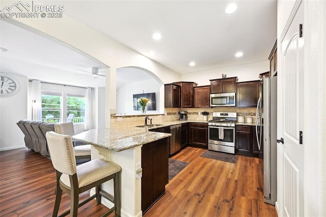 1914 Birmingham Loop, Colorado Springs, CO 80910 - kitchen with appliances with stainless steel finishes, dark brown cabinets, decorative backsplash, a peninsula, and light stone counters
