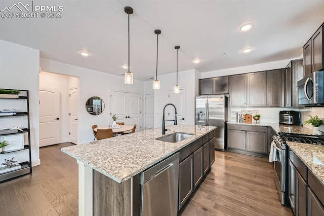 1851 Spring Water Pt, Colorado Springs, CO 80908 - kitchen with appliances with stainless steel finishes, wood finished floors, dark brown cabinetry, light stone countertops, and an island with sink