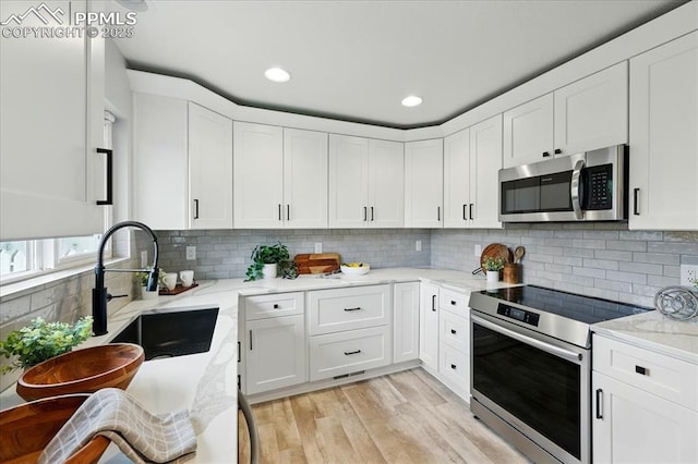 1112 Modes St, Colorado Springs, CO 80904 - kitchen with stainless steel appliances, white cabinets, light wood-type flooring, a sink, and light stone countertops