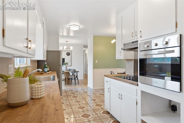 1411 Acacia Dr, Colorado Springs, CO 80907 - kitchen with appliances with stainless steel finishes, under cabinet range hood, white cabinetry, and a chandelier