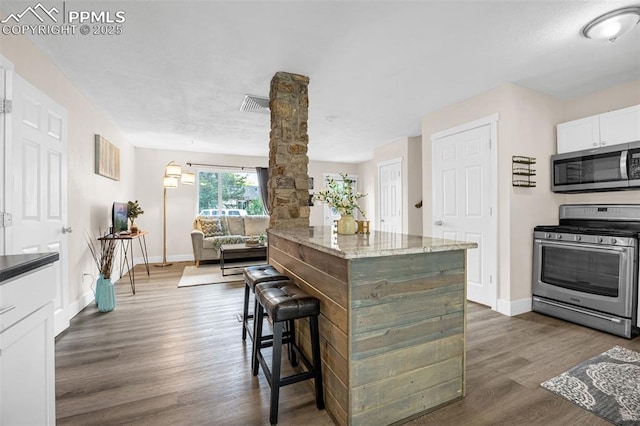 519 Crest St, Fountain, CO 80817 - kitchen featuring stainless steel appliances, dark wood finished floors, white cabinets, decorative columns, and a breakfast bar area