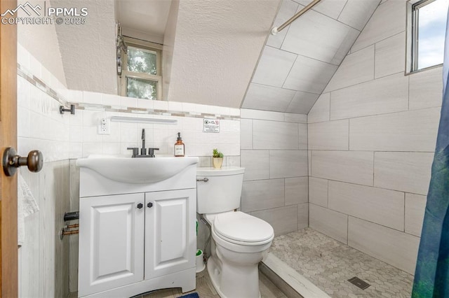 860 Golden Cycle Cir, Cripple Creek, CO 80813 - full bath with a tile shower, vaulted ceiling, vanity, a textured wall, and tile walls