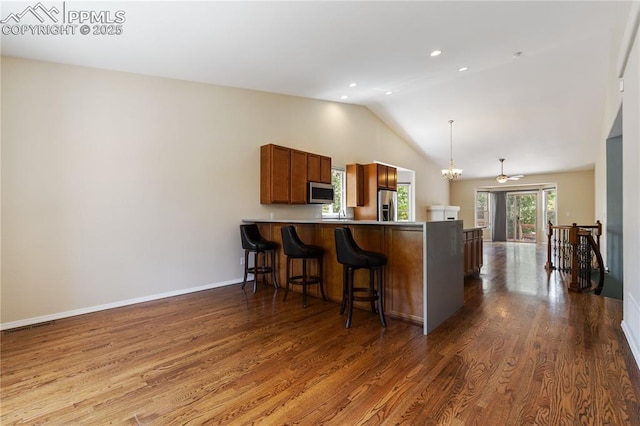 4410 Campus Bluffs Ct, Colorado Springs, CO 80918 - kitchen featuring appliances with stainless steel finishes, a peninsula, lofted ceiling, brown cabinets, and a breakfast bar