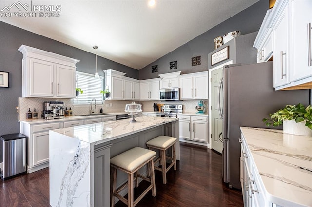 11310 Falling Star Rd, Fountain, CO 80817 - kitchen featuring stainless steel appliances, lofted ceiling, tasteful backsplash, a center island, and white cabinets