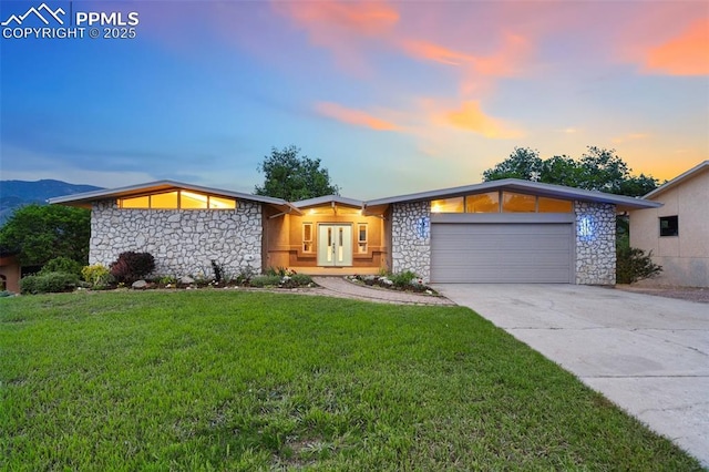 702 Crown Ridge Dr, Colorado Springs, CO 80904 - mid-century modern home featuring stone siding, an attached garage, concrete driveway, a lawn, and french doors