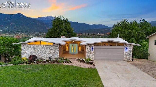702 Crown Ridge Dr, Colorado Springs, CO 80904 - mid-century modern home featuring stone siding, a mountain view, an attached garage, and a yard