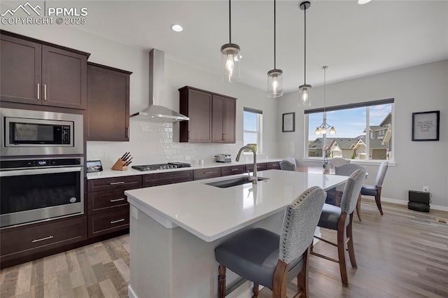 10076 Oro Belle Ct, Colorado Springs, CO 80924 - kitchen with stainless steel appliances, wall chimney exhaust hood, light wood-type flooring, light countertops, and a kitchen island with sink