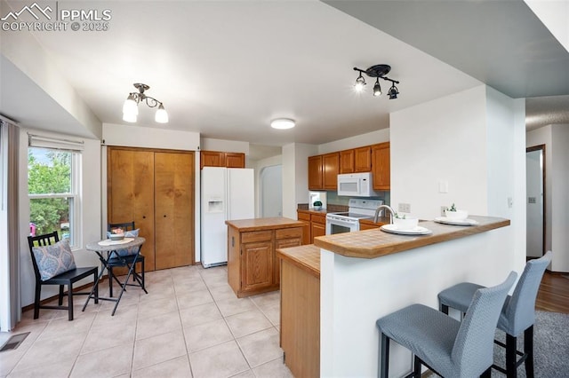2035 Springcrest Rd, Colorado Springs, CO 80920 - kitchen with white appliances, a peninsula, a breakfast bar, a kitchen island, and brown cabinets