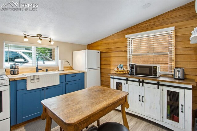 244 Washington St, Monument, CO 80132 - kitchen featuring blue cabinetry, white appliances, vaulted ceiling, wooden walls, and butcher block countertops