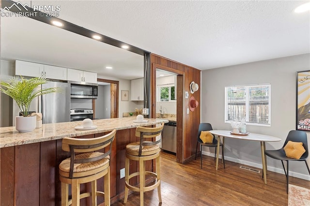 121 Via, San Miguel, Manitou Springs, CO 80829 - kitchen featuring appliances with stainless steel finishes, white cabinets, dark wood-style floors, a textured ceiling, and light stone counters