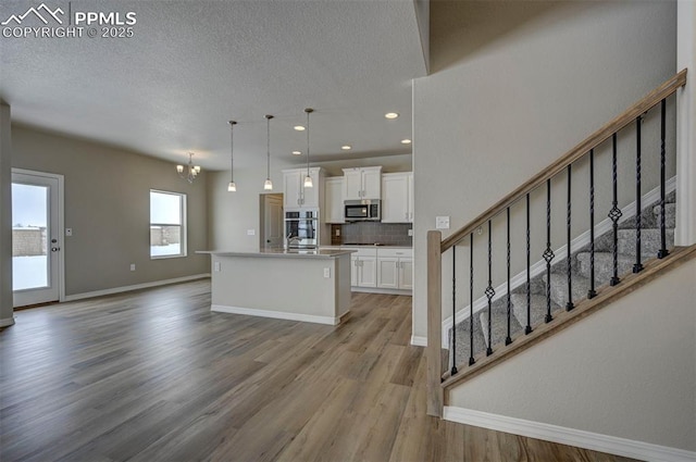 8235 Kittrick Pl, Falcon, CO 80831 - kitchen featuring appliances with stainless steel finishes, white cabinets, wood finished floors, an island with sink, and tasteful backsplash
