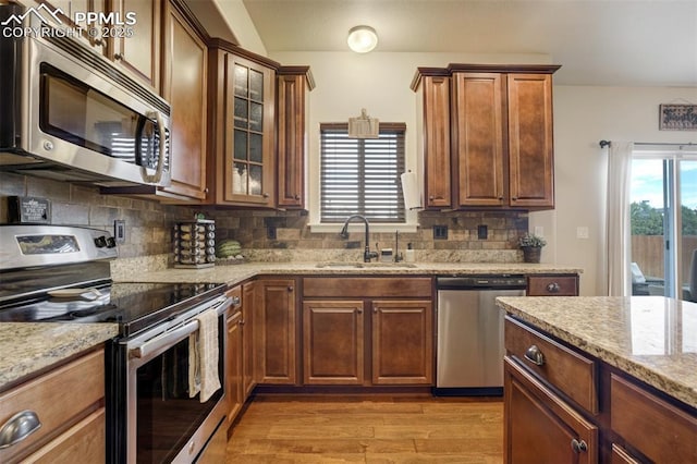10280 Abrams Dr, Colorado Springs, CO 80925 - kitchen with appliances with stainless steel finishes, light stone counters, light wood-style flooring, decorative backsplash, and glass insert cabinets