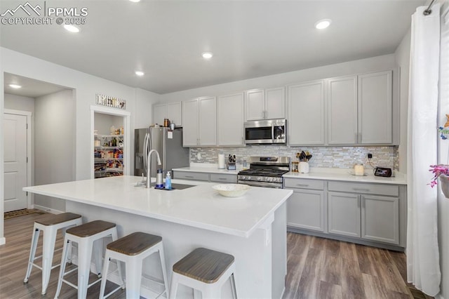 8101 Goldenray Pl, Colorado Springs, CO 80908 - kitchen with appliances with stainless steel finishes, wood finished floors, tasteful backsplash, a breakfast bar, and recessed lighting