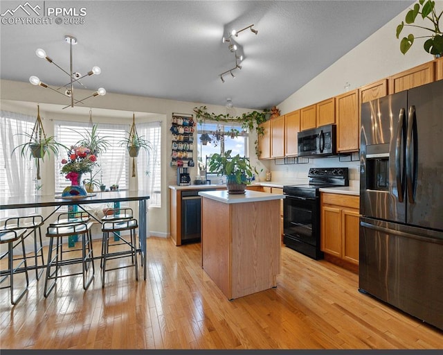 6355 Casual Dr, Colorado Springs, CO 80923 - kitchen with black appliances, a kitchen island, light countertops, vaulted ceiling, and light wood-style flooring