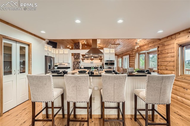 1527 S Pine Dr, Bailey, CO 80421 - kitchen featuring island exhaust hood, appliances with stainless steel finishes, white cabinetry, rustic walls, and a kitchen bar