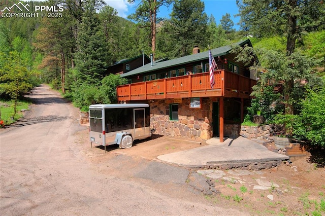 9615 Mountain Rd, Cascade, CO 80809 - view of front of home with a chimney, stone siding, a view of trees, and a wooden deck
