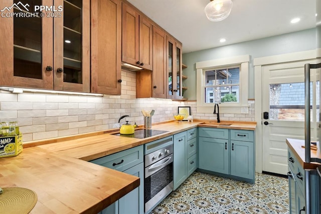 1401 N Tejon St, Colorado Springs, CO 80907 - kitchen featuring wooden counters, stainless steel oven, black electric stovetop, glass insert cabinets, and tasteful backsplash
