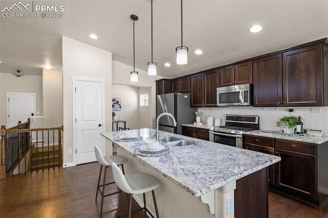 5060 Galloping Goose Way, Colorado Springs, CO 80924 - kitchen with appliances with stainless steel finishes, dark wood-style flooring, dark brown cabinets, an island with sink, and backsplash