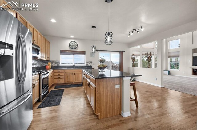 7665 Manston Dr, Colorado Springs, CO 80920 - kitchen featuring stainless steel appliances, a kitchen bar, dark countertops, light wood-style floors, and a kitchen island