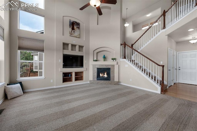 7665 Manston Dr, Colorado Springs, CO 80920 - unfurnished living room featuring carpet, a towering ceiling, ceiling fan, stairway, and a glass covered fireplace