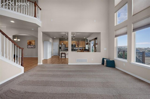 7665 Manston Dr, Colorado Springs, CO 80920 - unfurnished living room featuring a high ceiling, carpet flooring, stairs, arched walkways, and wood finished floors