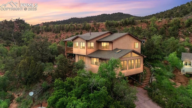 103 Pinon Ln, Manitou Springs, CO 80829 - back of property at dusk featuring a balcony, stairway, a wooded view, stucco siding, and a sunroom