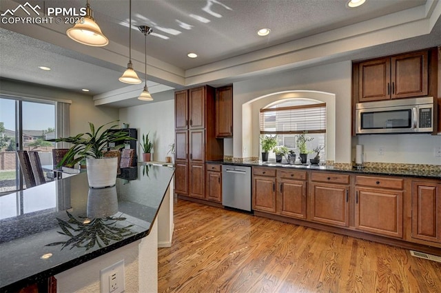 9444 Castle Oaks Dr, Fountain, CO 80817 - kitchen with appliances with stainless steel finishes, light wood-type flooring, a tray ceiling, decorative light fixtures, and dark stone counters