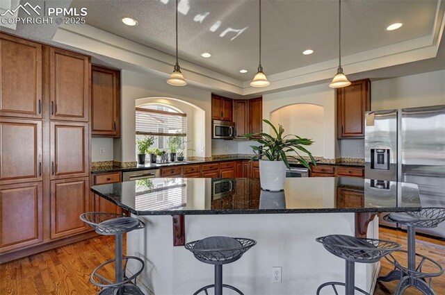 9444 Castle Oaks Dr, Fountain, CO 80817 - kitchen with stainless steel appliances, a raised ceiling, a center island, a kitchen bar, and arched walkways