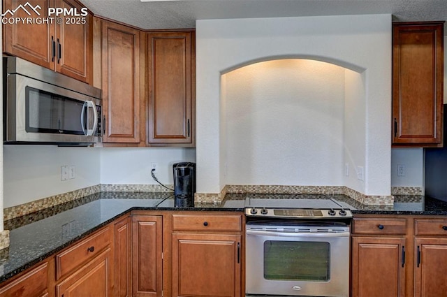 9444 Castle Oaks Dr, Fountain, CO 80817 - kitchen featuring stainless steel appliances, arched walkways, dark stone countertops, and brown cabinetry
