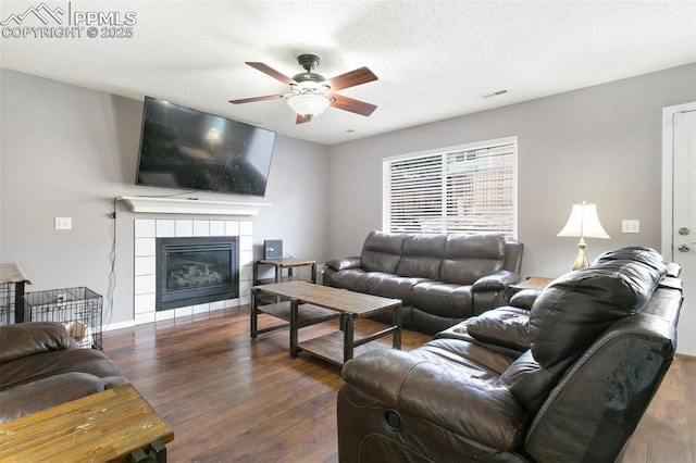 1360 Piros Dr, Colorado Springs, CO 80922 - living room featuring ceiling fan, dark wood finished floors, a tiled fireplace, and a textured ceiling