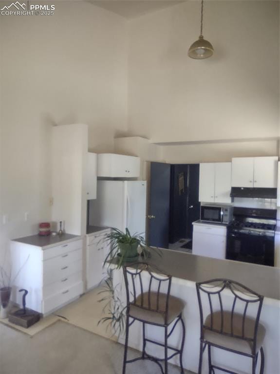 423 Ridge Rd, Divide, CO 80814 - kitchen featuring stove, stainless steel microwave, freestanding refrigerator, white cabinetry, and a kitchen breakfast bar