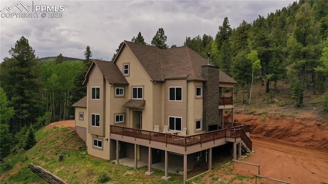 1522 Monarch Dr, Cripple Creek, CO 80813 - rear view of property with stucco siding, a deck, roof with shingles, and a wooded view