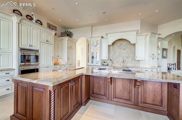 910 Grey Mountain Pt, Colorado Springs, CO 80906 - kitchen with arched walkways, stainless steel appliances, decorative backsplash, light stone counters, and a spacious island