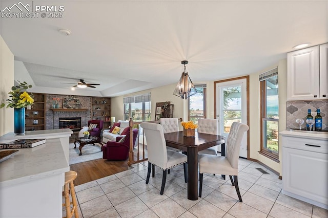 2505 Wimbleton Ct, Colorado Springs, CO 80920 - dining room featuring light tile patterned flooring, a brick fireplace, a chandelier, ceiling fan, and built in shelves