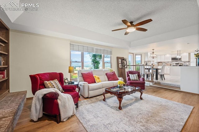 2505 Wimbleton Ct, Colorado Springs, CO 80920 - living room featuring ceiling fan, light wood finished floors, a textured ceiling, a chandelier, and a raised ceiling