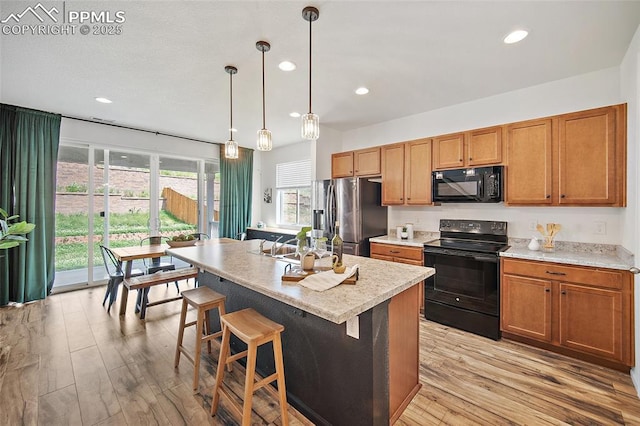 4867 Wolf Moon Dr, Colorado Springs, CO 80911 - kitchen with black appliances, light wood-style floors, recessed lighting, brown cabinetry, and an island with sink