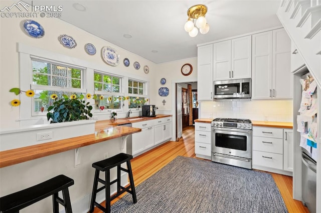 13 2nd St, Colorado Springs, CO 80906 - kitchen with butcher block countertops, appliances with stainless steel finishes, decorative backsplash, a breakfast bar, and light wood finished floors