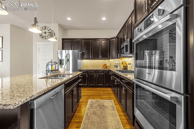 4187 Notch Trl, Colorado Springs, CO 80924 - kitchen featuring appliances with stainless steel finishes, light wood finished floors, light stone countertops, tasteful backsplash, and dark brown cabinets