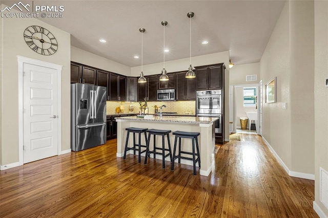 4187 Notch Trl, Colorado Springs, CO 80924 - kitchen with appliances with stainless steel finishes, dark wood finished floors, decorative backsplash, a breakfast bar, and dark brown cabinets