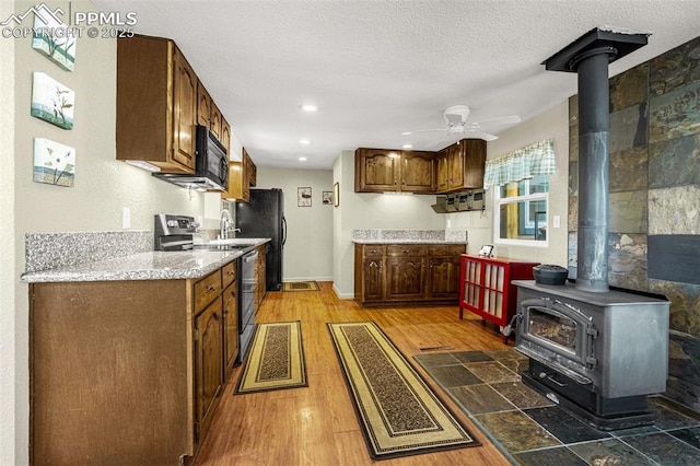 269 Evergreen Rd, Woodland Park, CO 80863 - kitchen featuring black appliances, a wood stove, ceiling fan, light wood-style floors, and a textured ceiling