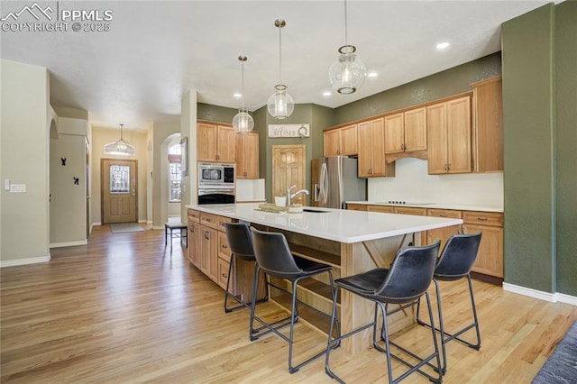 5763 Show Down Ln, Colorado Springs, CO 80923 - kitchen with stainless steel appliances, arched walkways, light wood finished floors, a kitchen breakfast bar, and light countertops