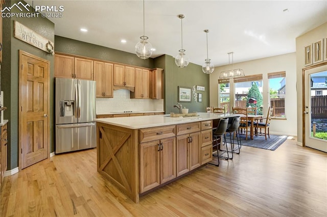 5763 Show Down Ln, Colorado Springs, CO 80923 - kitchen with stainless steel refrigerator with ice dispenser, light wood finished floors, light countertops, tasteful backsplash, and a kitchen island with sink