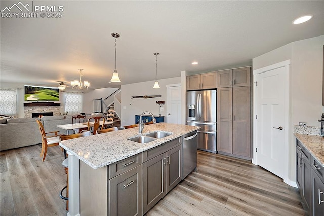 4928 Wolf Moon Dr, Colorado Springs, CO 80911 - kitchen featuring stainless steel appliances, a stone fireplace, a kitchen breakfast bar, light wood finished floors, and light stone countertops