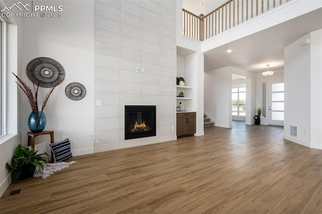 17226 Alsike Clover Ct, Monument, CO 80132 - unfurnished living room with wood finished floors, a tiled fireplace, stairs, built in features, and a high ceiling
