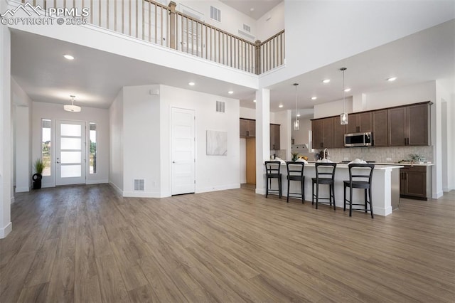 17226 Alsike Clover Ct, Monument, CO 80132 - kitchen featuring stainless steel microwave, a towering ceiling, light wood-style flooring, a breakfast bar, and dark brown cabinets