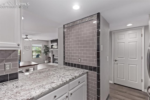 12183 W Chenango Dr, Morrison, CO 80465 - kitchen featuring a fireplace, white cabinetry, light stone countertops, dark wood-style floors, and a ceiling fan