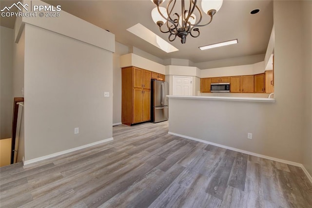 6872 Los Reyes Cir, Colorado Springs, CO 80918 - kitchen with appliances with stainless steel finishes, brown cabinetry, a chandelier, and light wood-style flooring