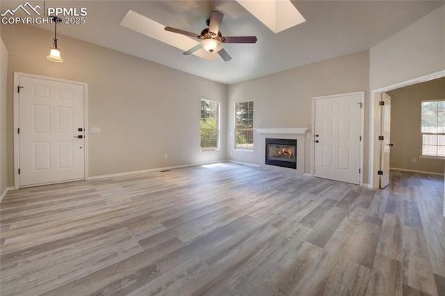 6872 Los Reyes Cir, Colorado Springs, CO 80918 - unfurnished living room featuring light wood finished floors, a glass covered fireplace, ceiling fan, and a skylight