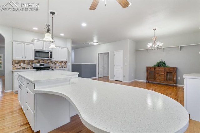 10489 Cedar Breaks Dr, Peyton, CO 80831 - kitchen with stainless steel appliances, arched walkways, white cabinets, decorative backsplash, and a large island
