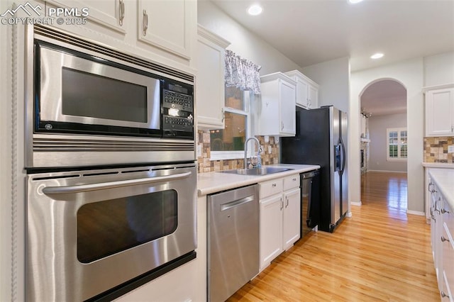 10489 Cedar Breaks Dr, Peyton, CO 80831 - kitchen with stainless steel appliances, arched walkways, backsplash, white cabinets, and light wood-style floors